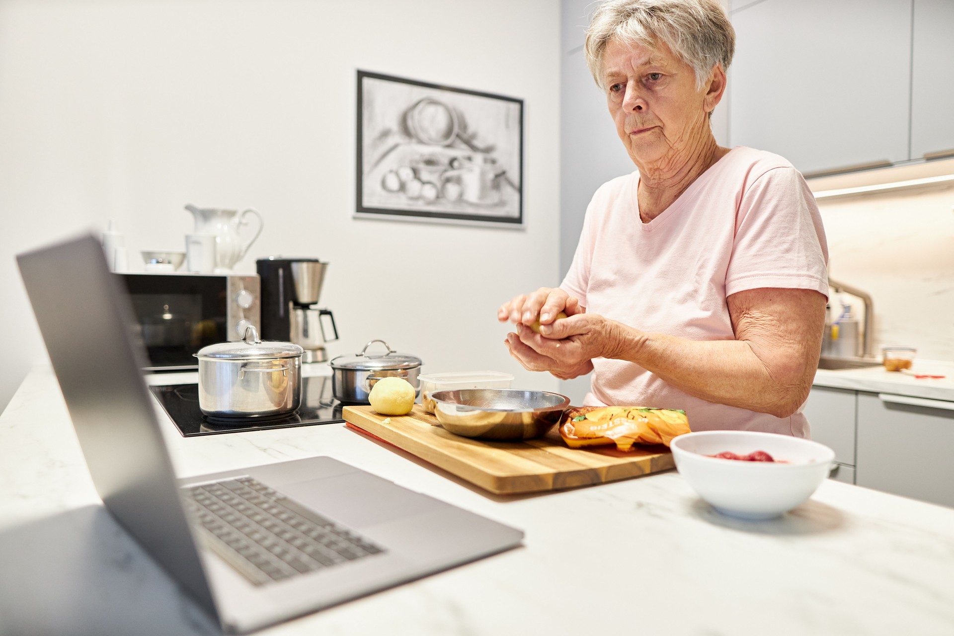 An 80-year-old senior citizen takes part in cooking classes online and uses her laptop or Macbook to cook in her own modern design kitchen An 80-year-old senior citizen takes part in cooking classes online and uses her laptop or Macbook to cook in her own modern design kitchen